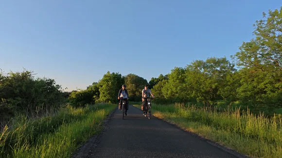 Radfahrende auf asphaltiertem Weg mit grünen Bäumen im Hintergrund bei sonnigem Wetter.