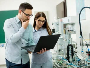 Young couple of students with laptop at robotics lab