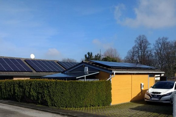 Das Foto zeigt ein E-Auto, das neben einem Gebäude mit Solarmodulen geparkt ist und über einen Anschluss am Gebäude aufgeladen wird.