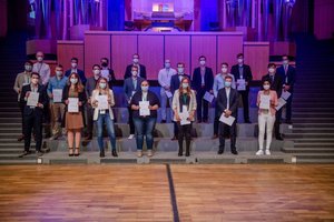 Absolvierende auf der Treppe vor der Orgel im Audimax mit Urkunde und Maske (Foto:RUB/Marquard)