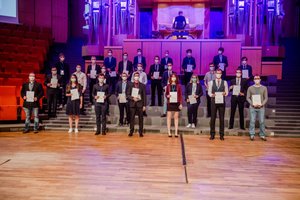 Absolvierende auf der Treppe vor der Orgel im Audimax mit Urkunde und Maske(Foto:RUB/Marquard)