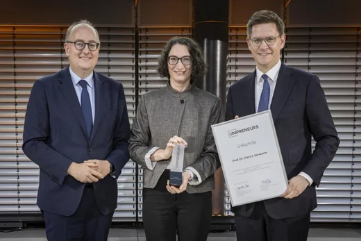 Auf dem Foto sind drei Personen zu sehen: Preisträgerin Clara Saraceno mit den Staatssekretären Matthias Hauer (BMFTR, links) und Johannes Steiniger (BMWE). 